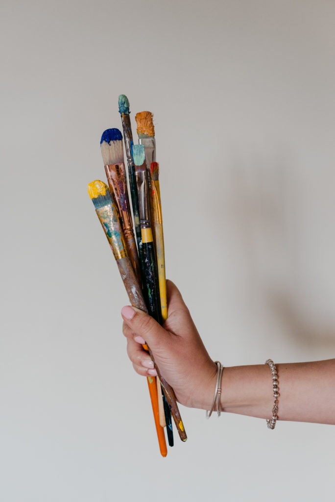 woman holding a bunch of paint brushes against a blank wall