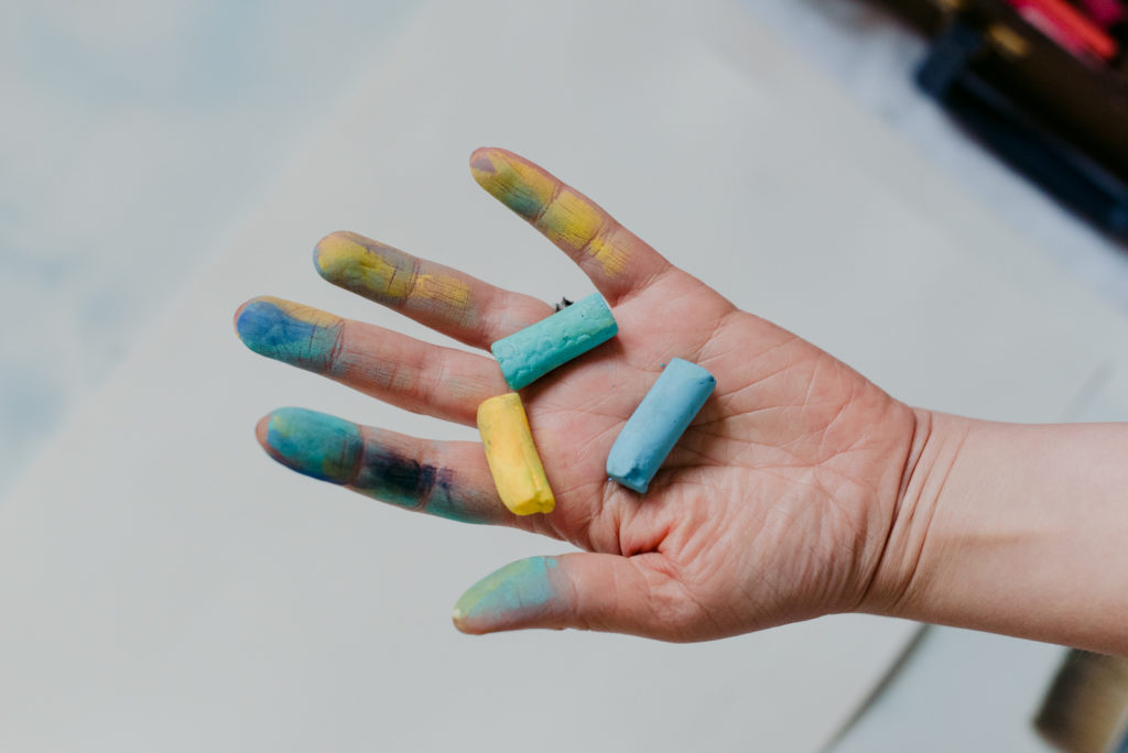 woman's hand holding blue and yellow pastels