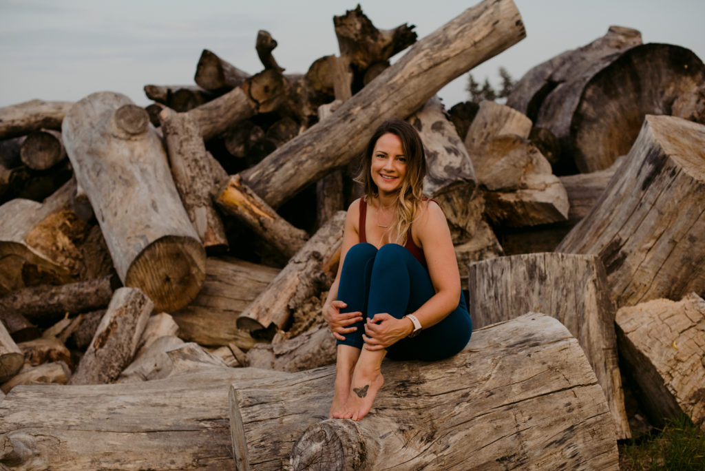 ottawa yoga teacher sitting on stack of logs smiling at the camera