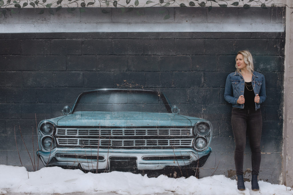 girl leaning against mural wall with old vintage car