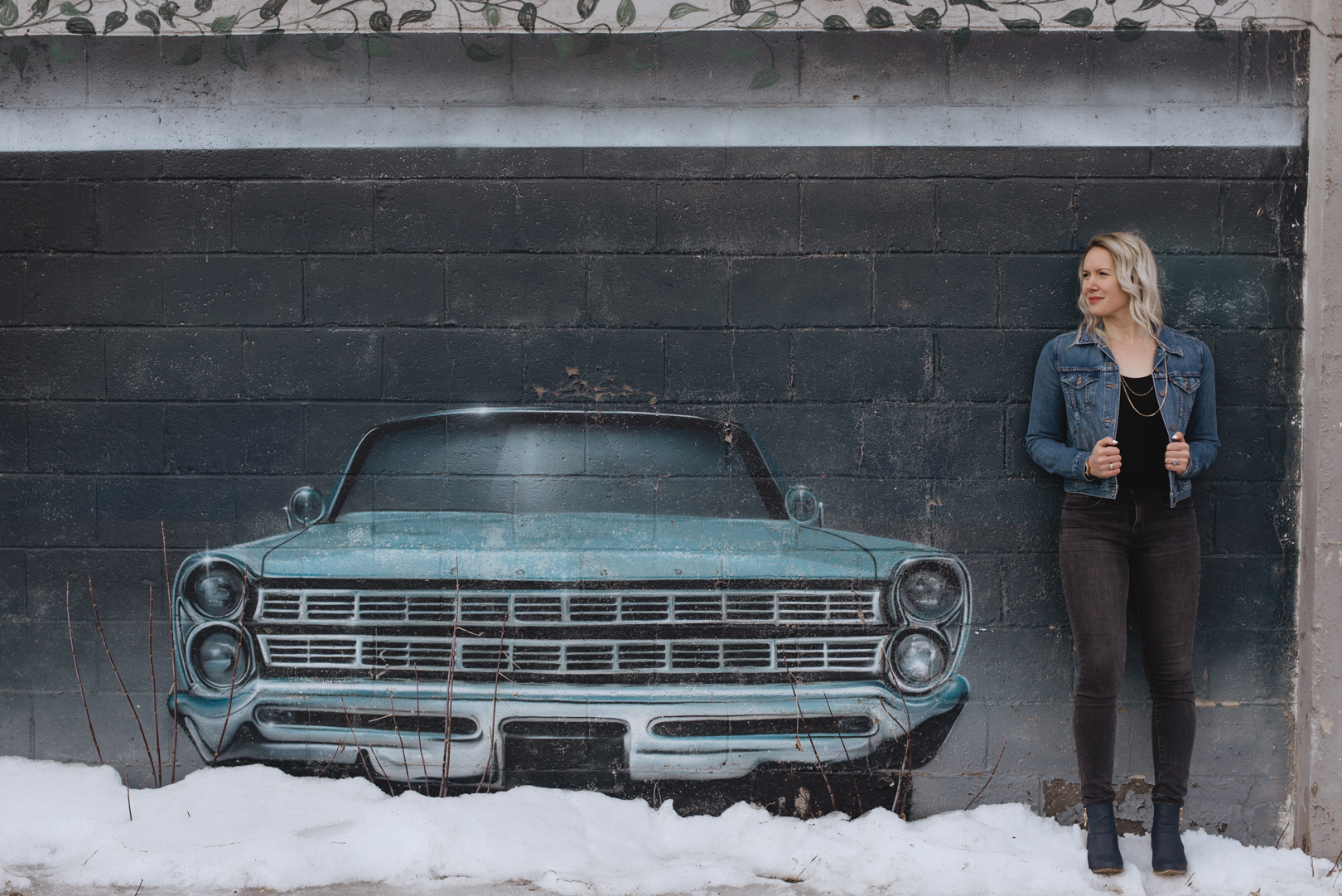 girl leaning against mural wall with old vintage car