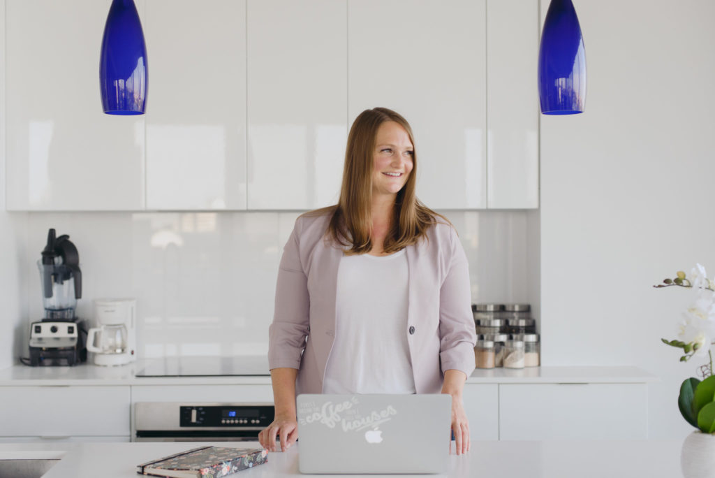 real estate agent standing in a white kitchen with laptop looking out the window