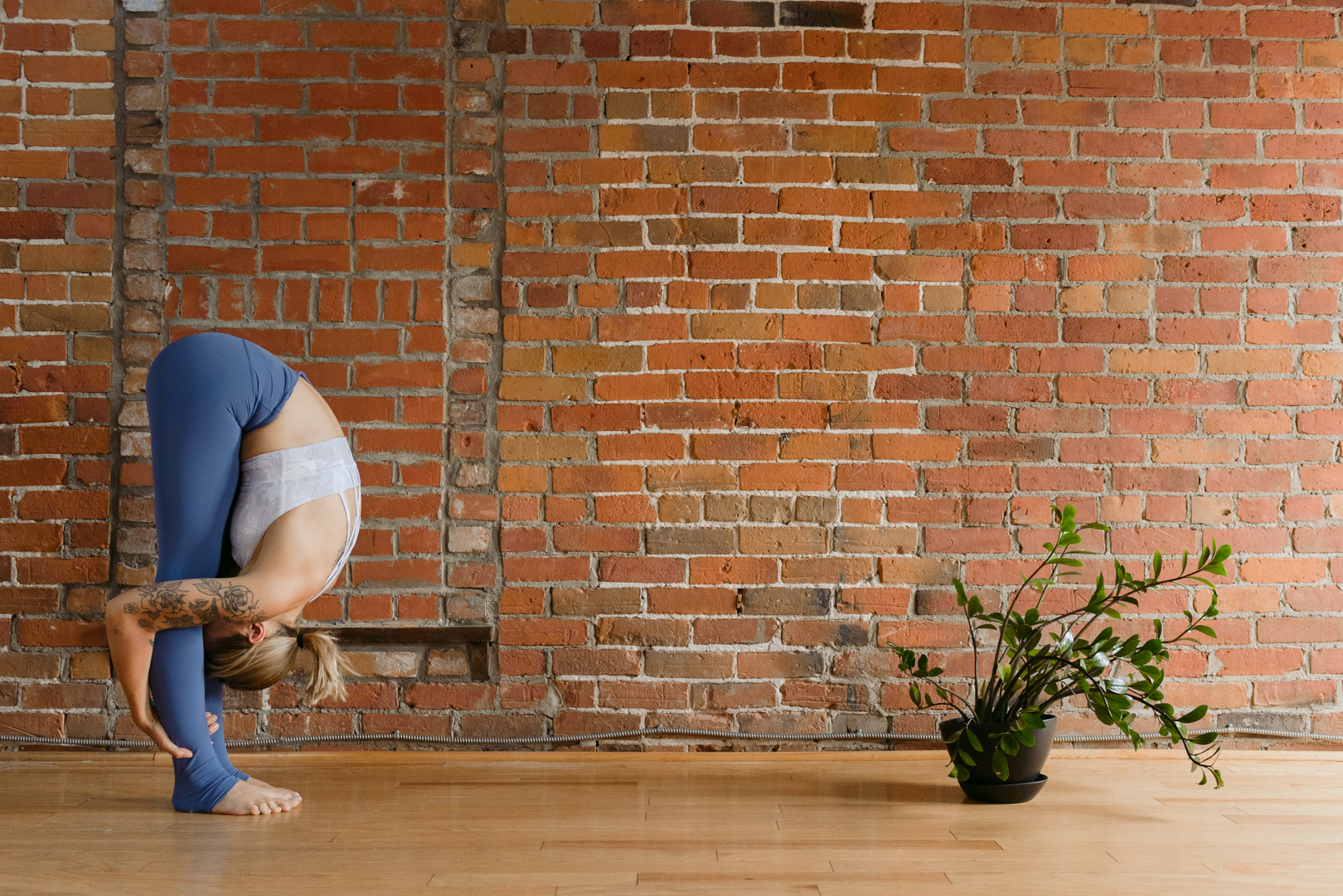 yoga teacher in standing forward fold against red brick wall