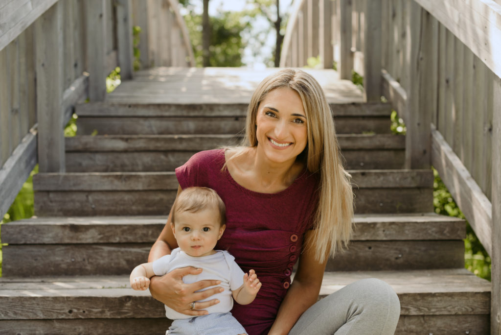 registered nurse with baby smiling at the camera while sitting on the stairs