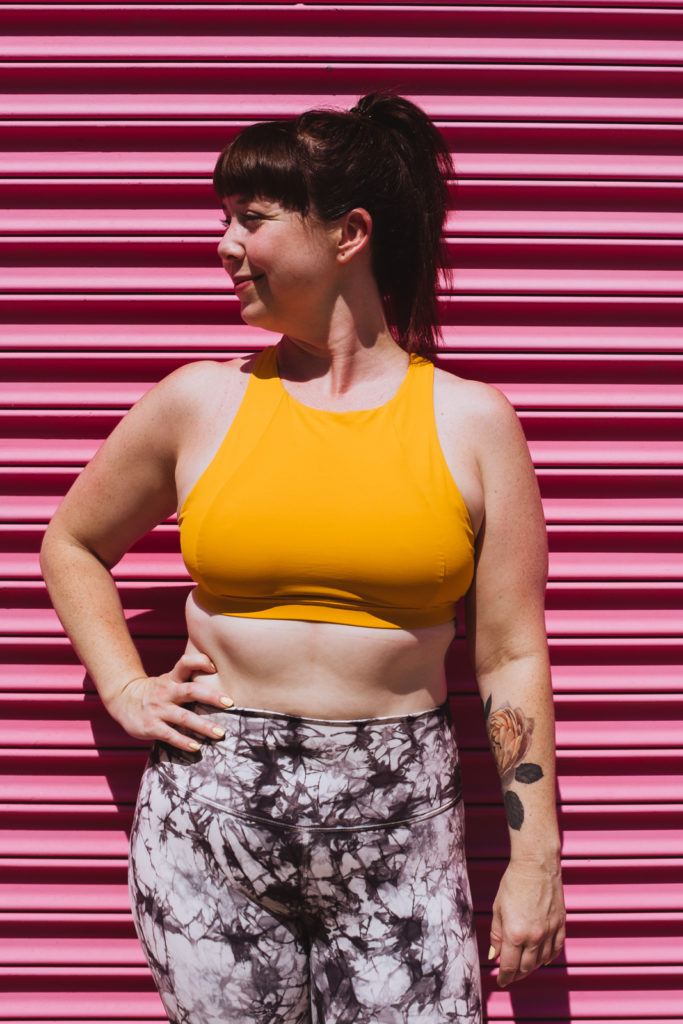 yoga teacher in yellow tank against bright pink wall