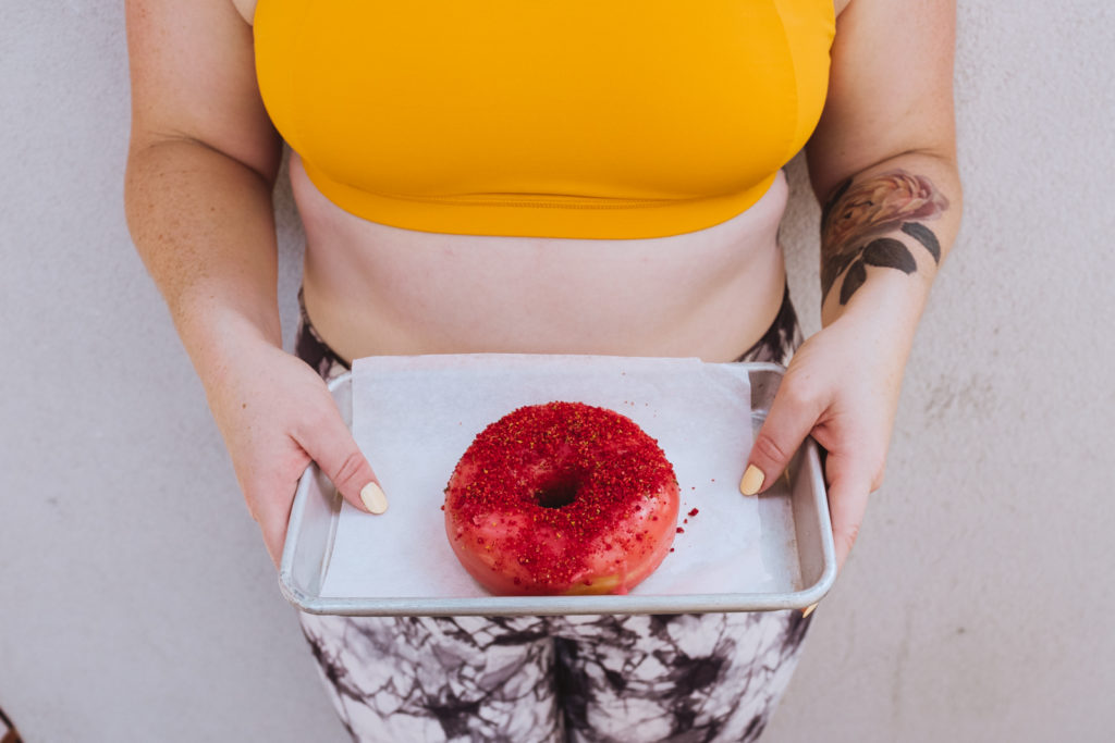 yoga teacher holding bright pink donut in yellow top