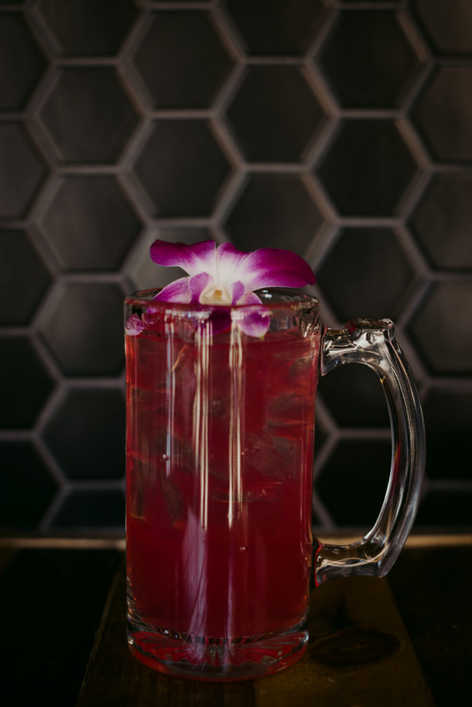 pink cocktail with orchid against black tile wall
