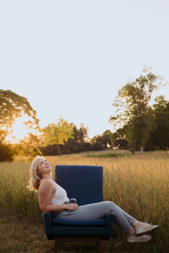 girl in white tank top sitting on blue chair in field at sunset