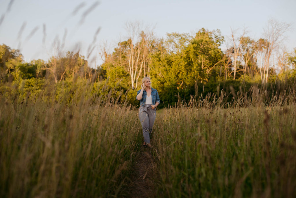 blonde girl in jean jacket standing in a field at sunset