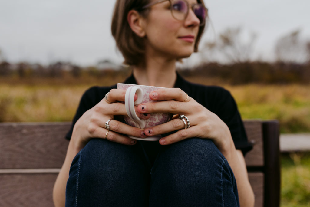 copywriter with chipped nail polish holding a coffee mug sitting on a bench in the fall