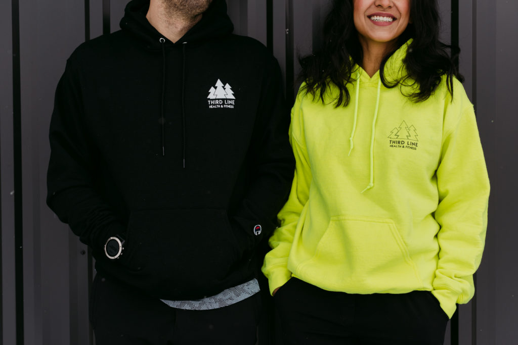 man and woman in hoodies standing against black wall