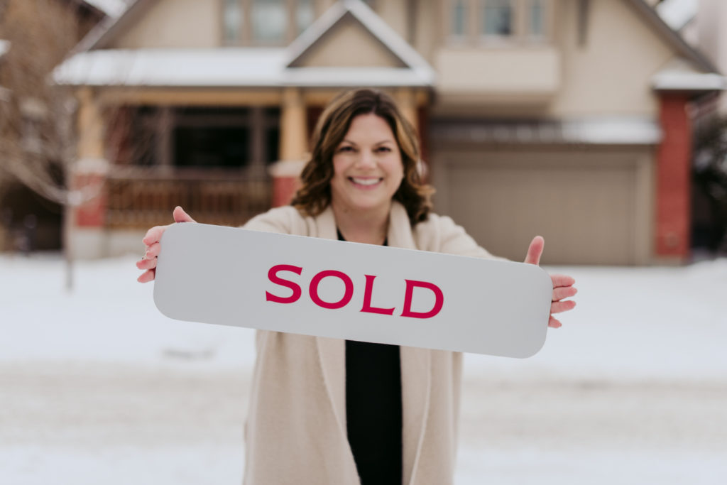 Daria Kark real estate agent holding sold sign in front of house