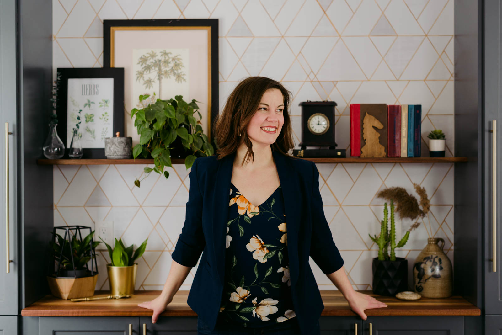 female entrepreneur standing in front of a wallpapered wall with shelf and books