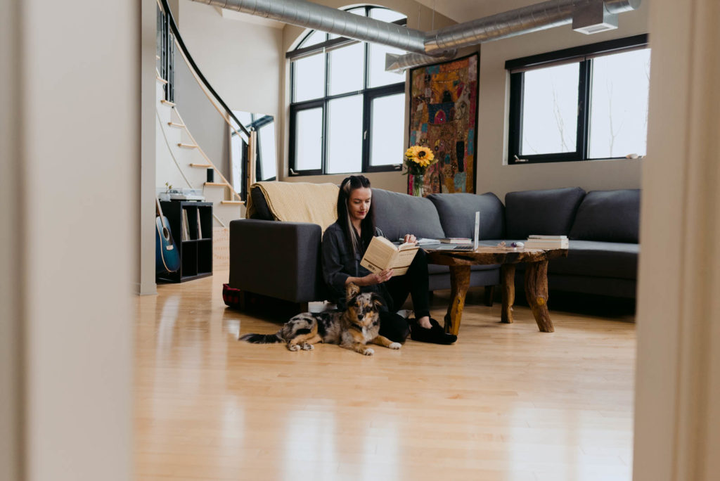 female entrepreneur sitting on the floor of her condo reading a book with her dog