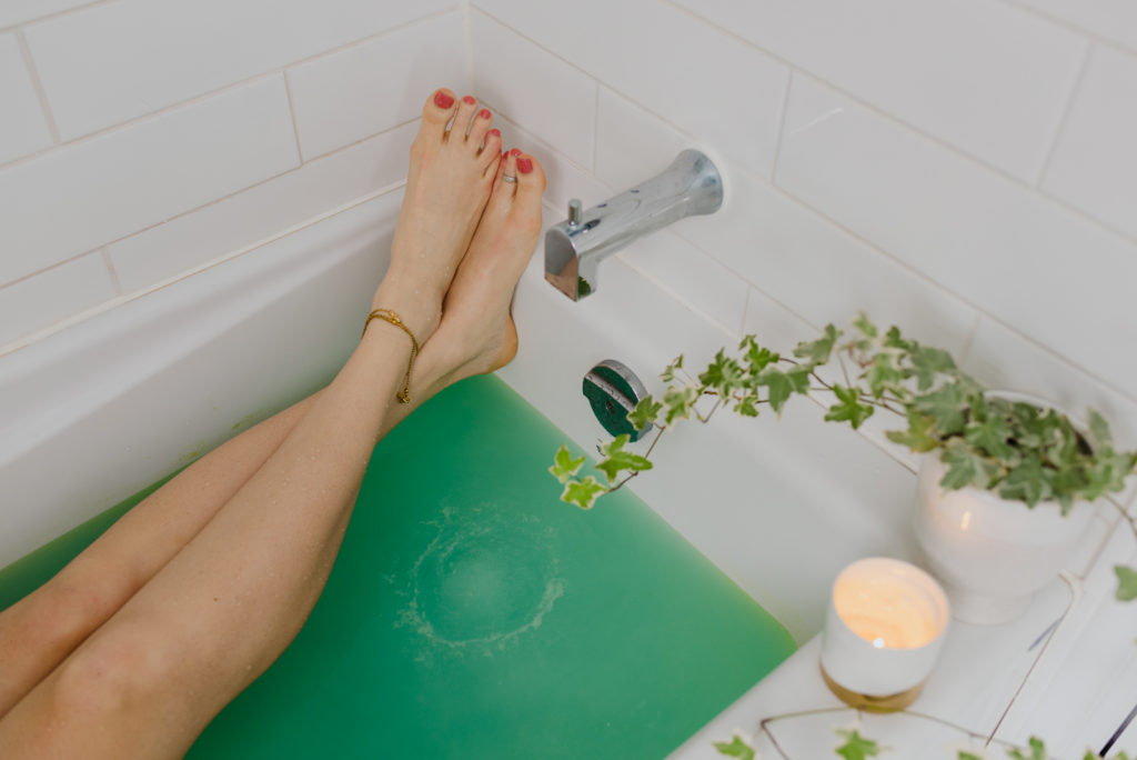 woman's legs in bath with green bath bomb in the water