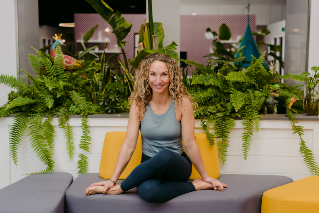 yoga teacher sitting on couch near plants smiling at the camera