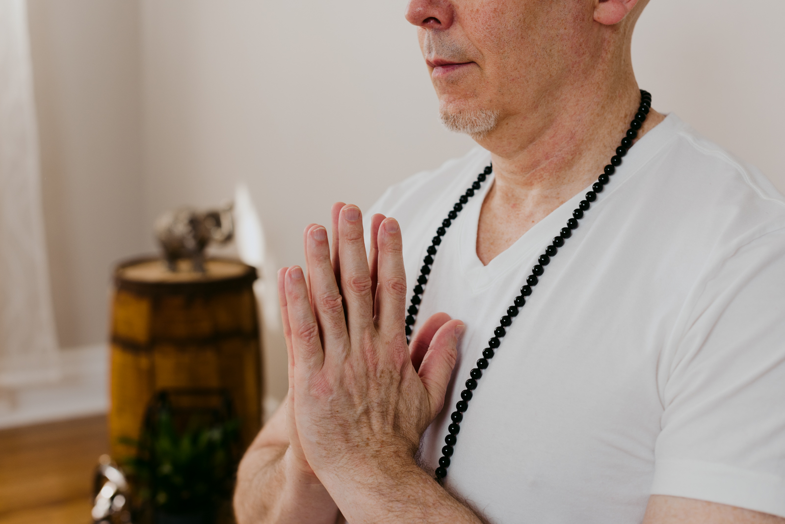 yoga teacher meditating with black mala on and hands at heart
