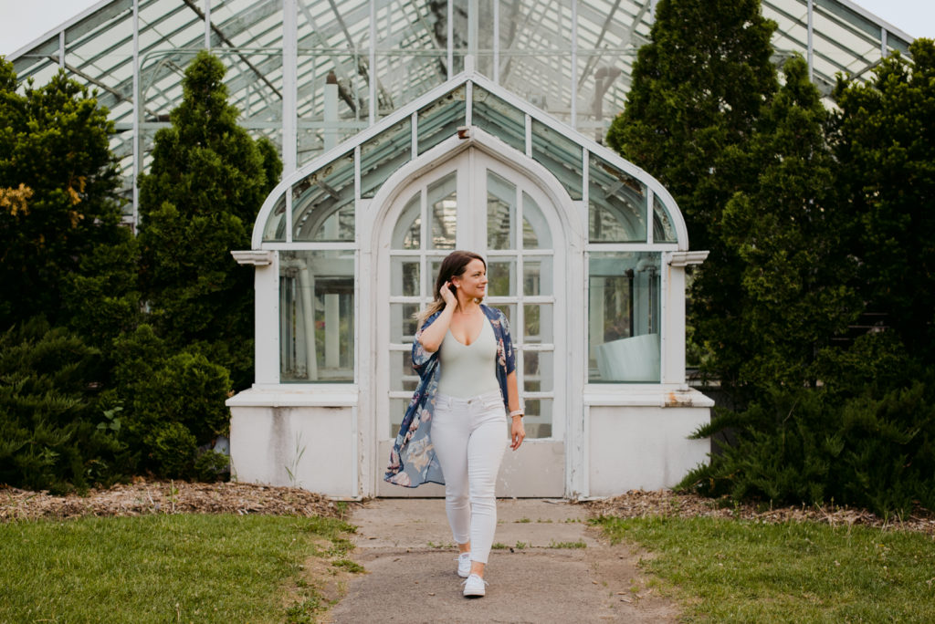 yoga teacher wearing street clothes walking in front of greenhouse