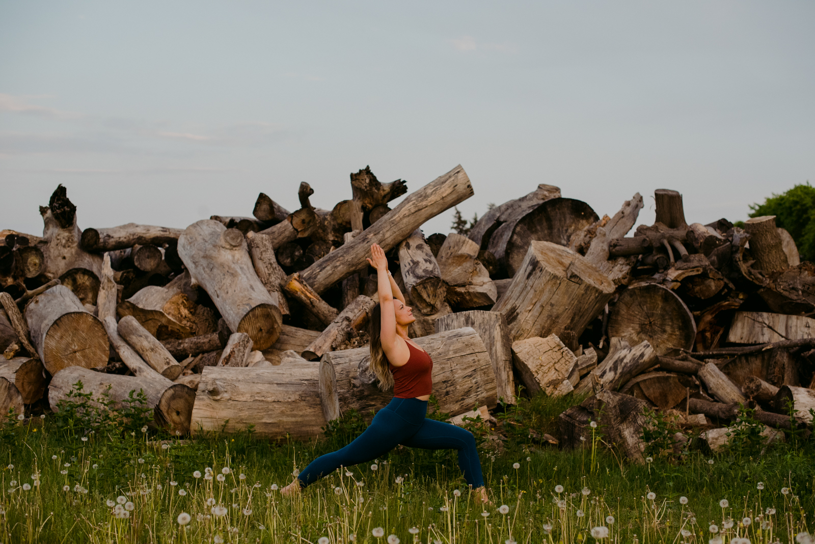 ottawa yoga teacher in crescent moon in front of stack of logs