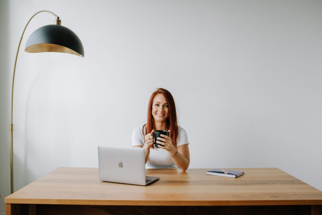 woman entrepreneur drinking coffee at a wooden desk with her laptop