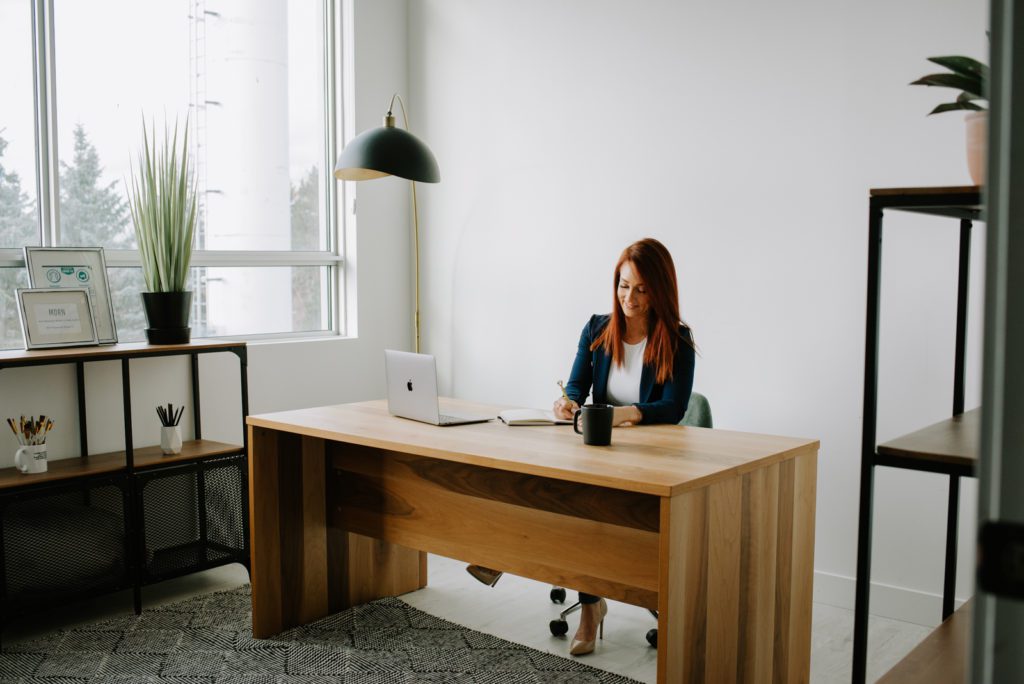 woman entrepreneur drinking coffee at a wooden desk with her laptop
