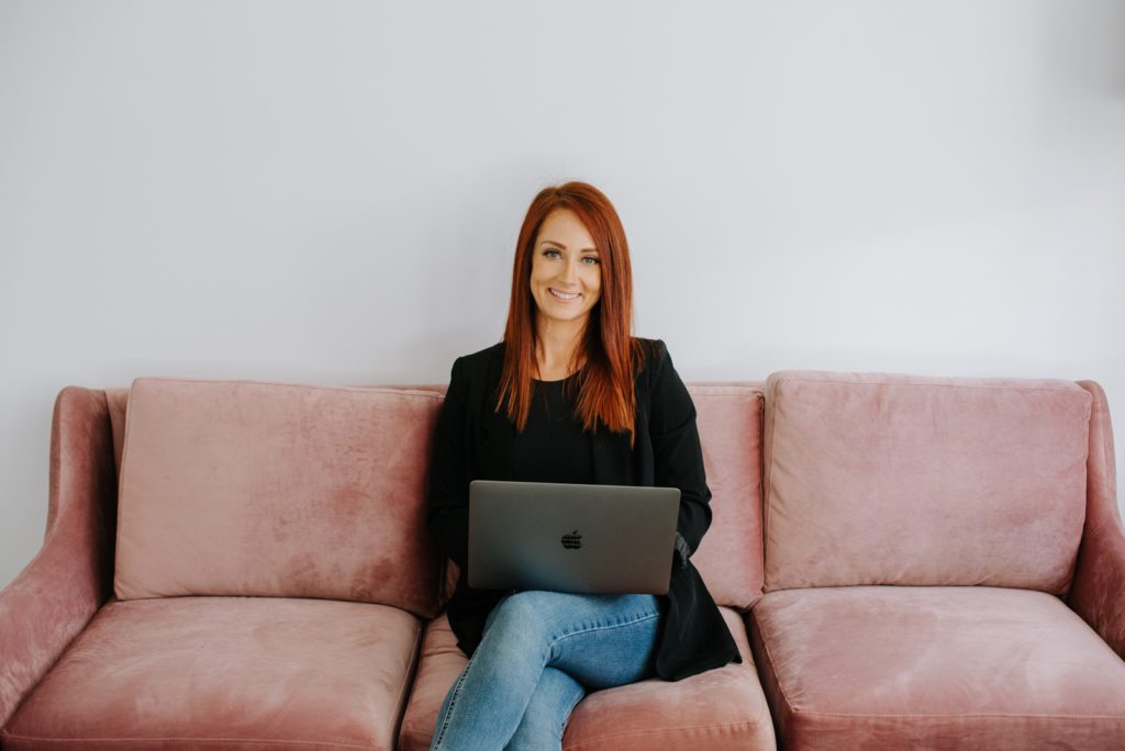 woman entrepreneur sitting on pink velvet couch with laptop